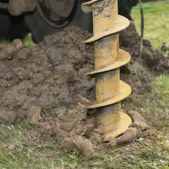Wiertnica zagłębia się w ziemię, przygotowując miejsce pod studnię głębinową 30m. Widać urobek ziemi i fragment maszyny.
