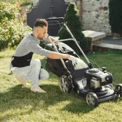 Mężczyzna w fartuchu sprawdza kosiarkę, zastanawiając się, na jaką wysokość kosić trawę, by ogród wyglądał idealnie.